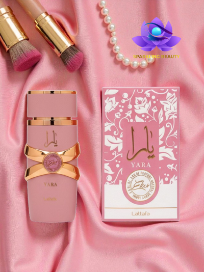 Perfume Yara da Lattafa com embalagem rosa e dourada numa superfície de tecido rosa com pincéis e colar de pérolas