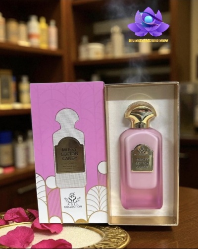 Frasco de perfume rosa fosco e caixa cor-de-rosa com texto, sobre mesa de madeira com prateleiras ao fundo