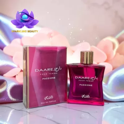 Frasco e caixa de perfume vinho DAAREJ Passione sobre superfície branca com tecidos rosados e lilás ao fundo.