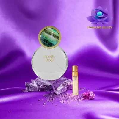 Frasco de perfume Pretty Doll com tampa verde e branco e frasco dourado pequeno sobre tecido roxo