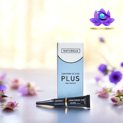 Creme para contorno dos olhos NATURNUA PLUS com embalagem e tubo preto com texto branco, sobre superfície reflexiva com flores cor-de-rosa e roxas