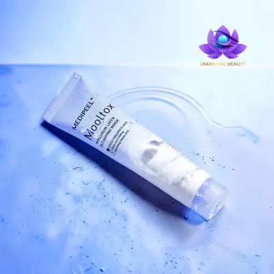 Tubo branco de máscara facial Mooltox sobre superfície azul molhada com logótipo Sparkling Beauty