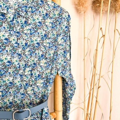 Vestido floral azul com cinto azul claro pendurado em cabide de madeira