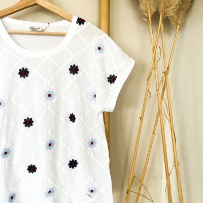T-shirt branca bordada com flores coloridas pendurada num cabide de madeira