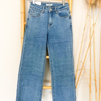 Calças de ganga azuis com bainha desfiada penduradas num cabide de madeira.