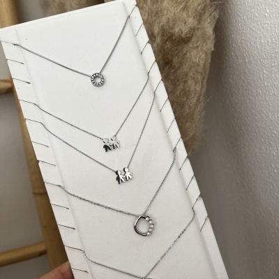 Conjunto de cinco colares em prata com diferentes pendentes em suporte branco.