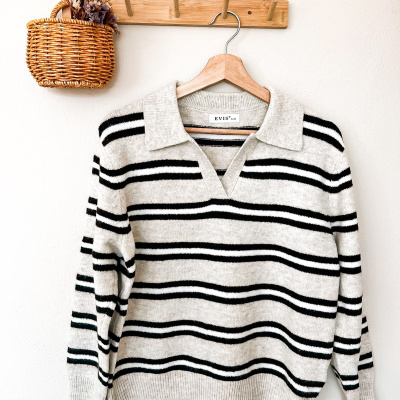 Camisola de malha listrada preta e creme pendurada num cabide de madeira com cabideiro e cesta de vime