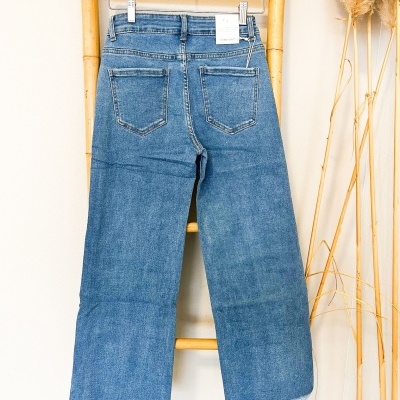 Calças de ganga azuis com bainha desfiada penduradas num cabide de madeira