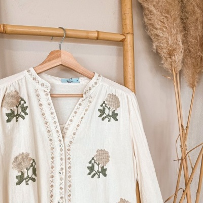 Blusa branca bordada com flores pendurada em cabide de madeira