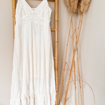 Vestido comprido branco com detalhes em renda pendurado em estrutura de bambu