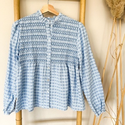 Blusa azul clara com padrão xadrez pendurada em escada de bambu com plantas secas ao lado