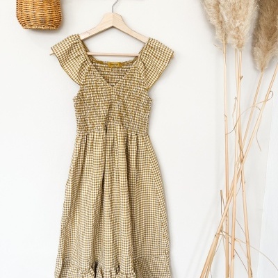 Vestido xadrez amarelo e branco em cabide de madeira na parede com decoração de flores secas