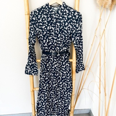 Vestido azul escuro com flores brancas pendurado numa escada de bambu.