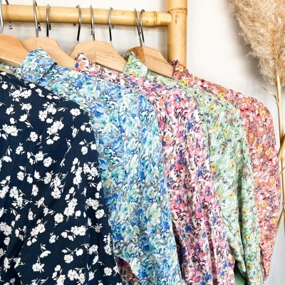 Camisas florais coloridas penduradas em cabides de madeira numa barra de bambu com decoração seca