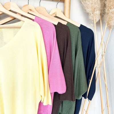 Cinco camisolas de malha coloridas penduradas em cabides de madeira