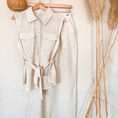 Conjunto de roupa bege claro pendurado com camisa e calças, decorado com cesta de vime e plantas secas