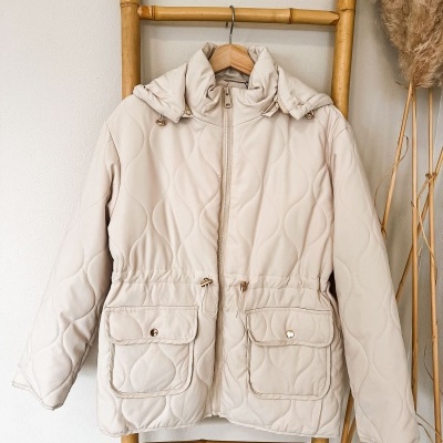 Casaco acolchoado bege claro com padrão em ondas pendurado numa estrutura de madeira de bambu