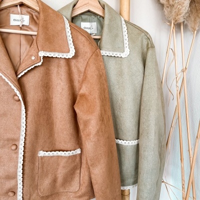 Duas casacas castanha e verde-acinzentada com bordados em renda branca penduradas num cabide de bambu.