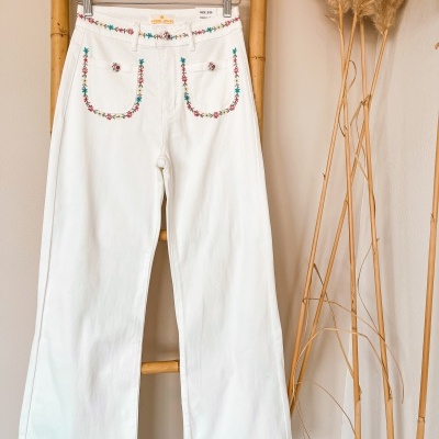 Calças brancas bordadas penduradas numa estrutura de bambu junto a plantas secas