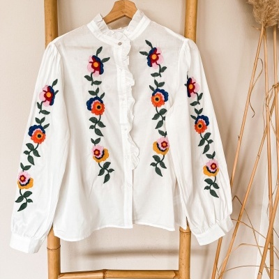Camisa branca de manga comprida com bordados florais coloridos.