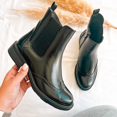 Botas Chelsea pretas em pele sobre fundo branco com decoração de plumas