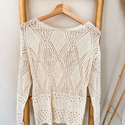 Camisola branca de malha rendada pendurada em cabide sobre estrutura de bambu.