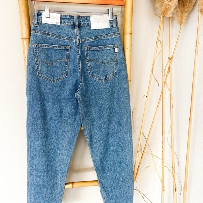 Calças de ganga azuis penduradas numa varinha de madeira clara com plantas decorativas secas ao lado