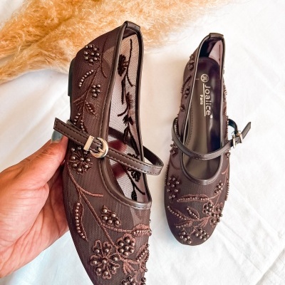 Par de sapatos castanhos com bordados florais e tira com fivela sobre fundo branco