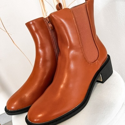 Botas de couro castanho com salto médio preto e elástico lateral castanho num banco branco