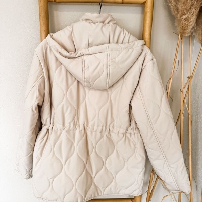 Casaco acolchoado bege claro com capuz pendurado numa escada de bambu