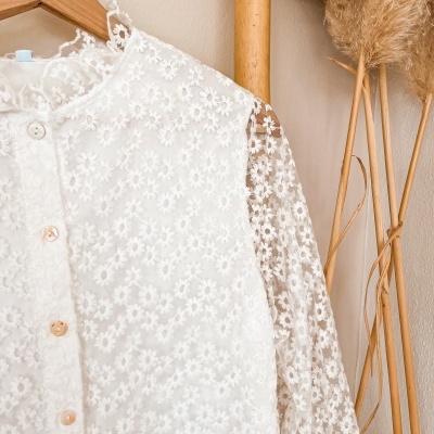 Blusa branca transparente com flores bordadas em cabide de madeira