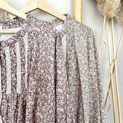 Dois vestidos florais com detalhes em renda pendurados em cabides de madeira