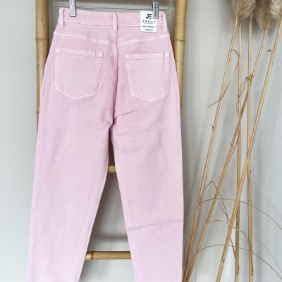 Calças rosa claro em tecido denim penduradas numa estrutura de bambu com etiqueta visível