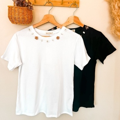 T-shirts branca e preta com decoração de flores penduradas em cabides de madeira