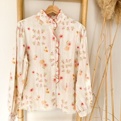 Blusa floral creme com folho vermelho pendurada numa estrutura de bambu