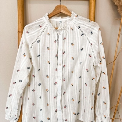 Camisa branca de manga comprida com bordados florais coloridos pendurada num cabide