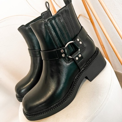 Botas pretas de couro com fivela metálica sobre banco branco