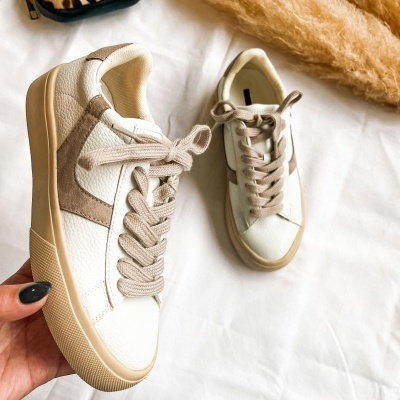 Sapatilhas brancas com detalhes em bege sobre tecido branco ao lado de bolsa pequena estampada de leopardo