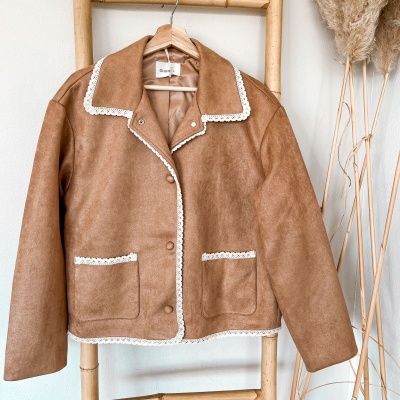 Casaco castanho com renda branca pendurado em cabide de madeira