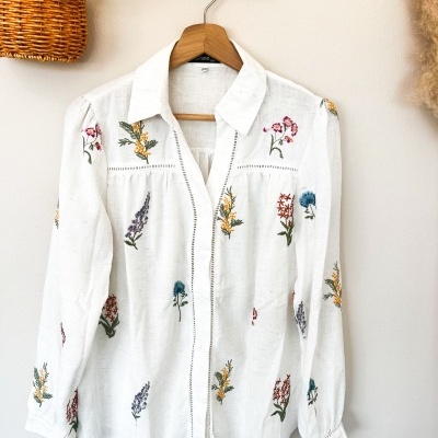 Camisa branca bordada floral pendurada num cabide de madeira