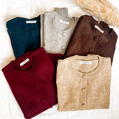 Cinco cardigans dobrados em várias cores com botões sobre fundo branco e ramos decorativos