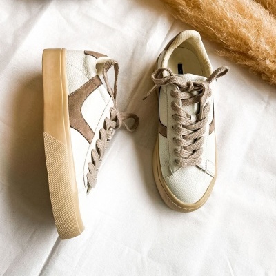 Ténis brancos com detalhes castanhos sobre tecido branco com bolsa de padrão animal print e planta seca