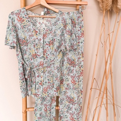 Conjunto feminino floral pendurado em estrutura de bambu com plantas secas ao lado