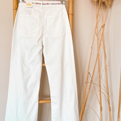 Calças brancas com bordado colorido penduradas numa estrutura de bambu