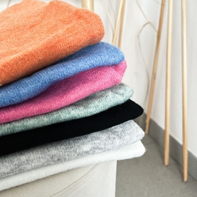 Pilhas de camisolas de malha coloridas sobre banco com pernas de madeira ao fundo