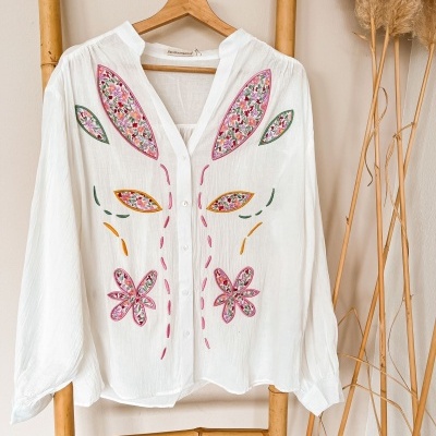 Camisa branca com bordados florais coloridos pendurada em cabide de madeira