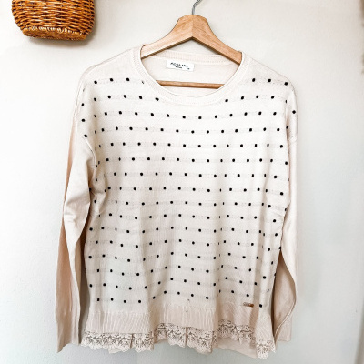 Camisola creme com padrão preto pendurada num cabide de madeira