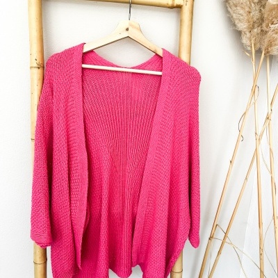 Cárdigan rosa pendurado em escada de bambu com ramos secos ao lado