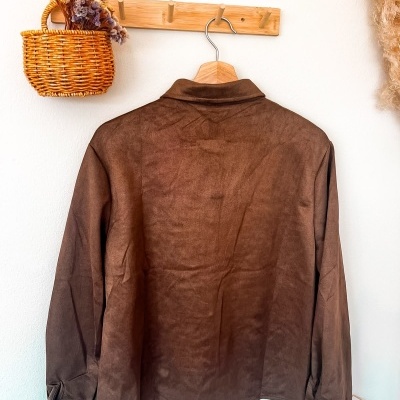 Camisa castanha aveludada pendurada num cabide de madeira num cabideiro de madeira com cesta de flores secas