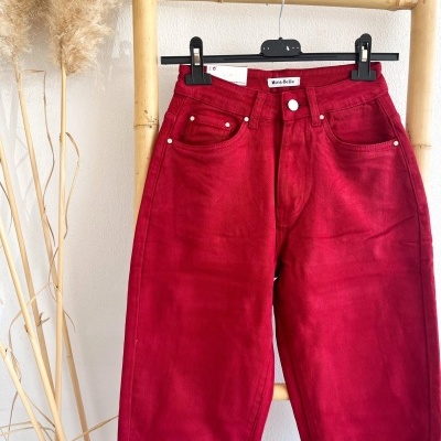 Calças vermelhas de ganga penduradas num cabide preto sobre estrutura de bambu